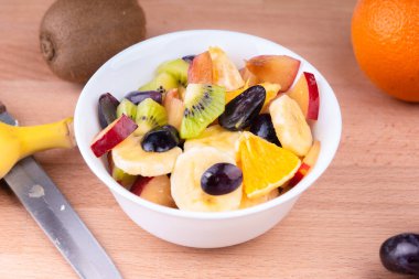 İçinde muz, üzüm, kivi, elma, portakal olan bir masada meyve salatası.