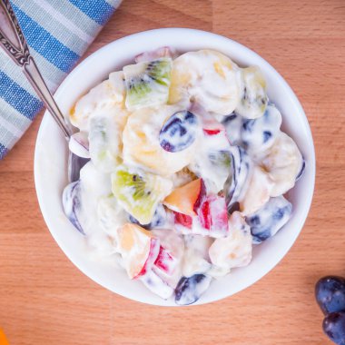 Meyve salatası ve Yunan yoğurdu. Yakın çekim, muz, üzüm, kivi, elma, portakal.