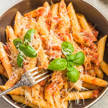 Fesleğen yapraklı bir tabakta domates ve sarımsak soslu sade İtalyan makarna. Yakın çekim, üst manzara.