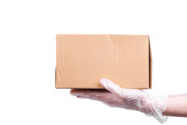 Female hand in a disposable transparent glove holds a cardboard box - safe delivery of goods, isolate on a white background, copy space