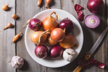 Eski bir ahşap masa üzerinde duran beyaz bir plaka farklı soğan ampuller birkaç tür.