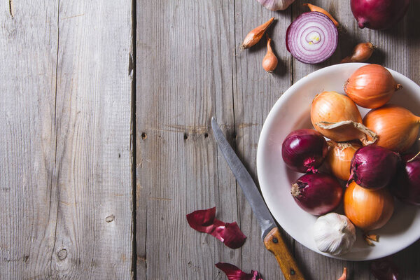 Несколько видов луковых луковиц на белой тарелке, стоящих на старом деревянном столе
.