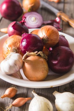 Eski bir ahşap masa üzerinde duran beyaz bir plaka farklı soğan ampuller birkaç tür.