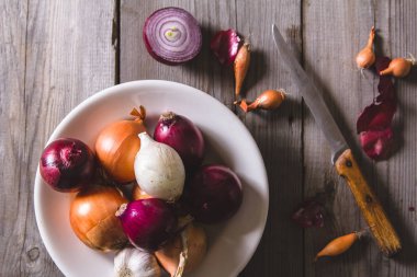 Eski bir ahşap masa üzerinde duran beyaz bir plaka farklı soğan ampuller birkaç tür.