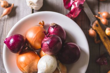 Eski bir ahşap masa üzerinde duran beyaz bir plaka farklı soğan ampuller birkaç tür.