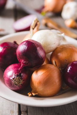 Eski bir ahşap masa üzerinde duran beyaz bir plaka farklı soğan ampuller birkaç tür.