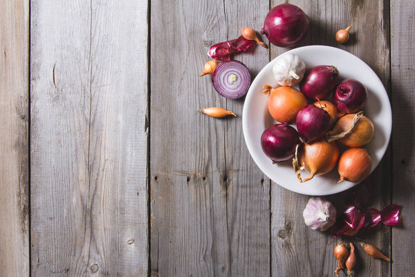Несколько видов луковых луковиц на белой тарелке, стоящих на старом деревянном столе
.
