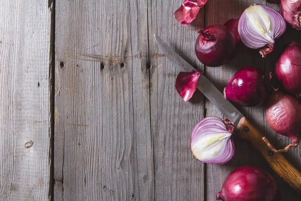 Rote Zwiebelzwiebeln liegen auf einem alten Holztisch. — Stockfoto