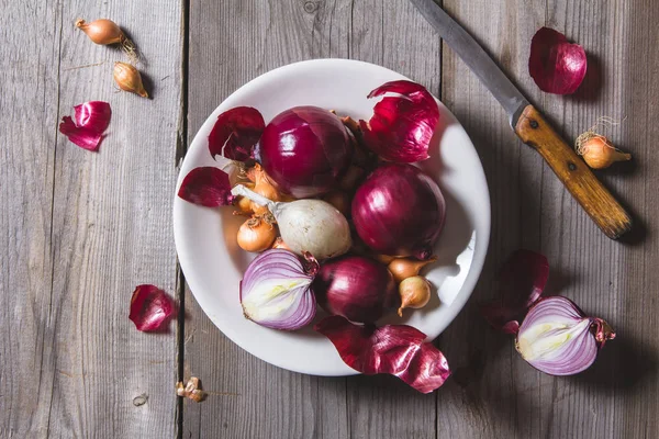 Verschiedene Zwiebelsorten auf einem weißen Teller, der auf einem alten Holztisch steht. — Stockfoto