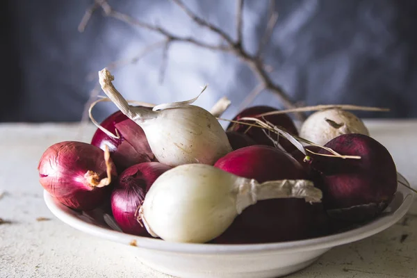 Ampoules à oignons rouges et blancs dans l'assiette sur une vieille table peinte en bois — Photo