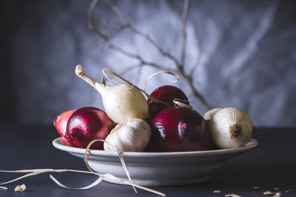 Red and white onion bulbs in the plate on black table