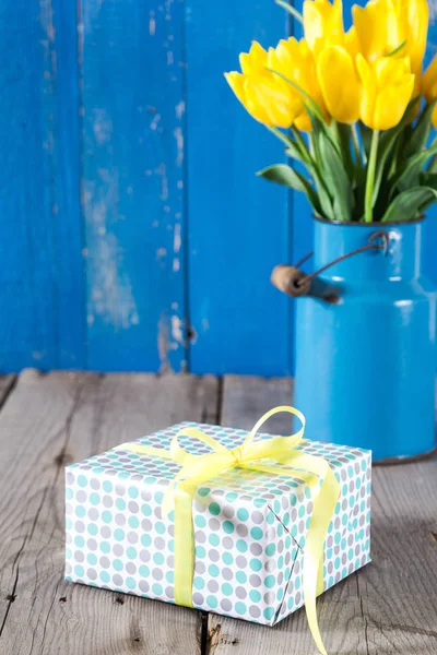 Bouquet of yellow tulips in vase and giftbox on a wooden background — Stock Photo, Image