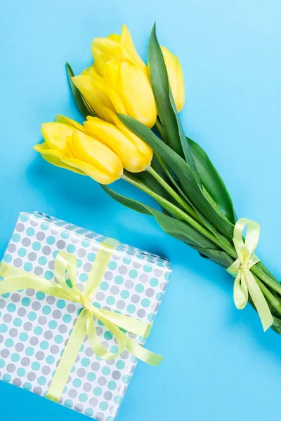 Bouquet de belles tulipes jaunes fraîches sur fond bleu et boîte cadeau — Photo