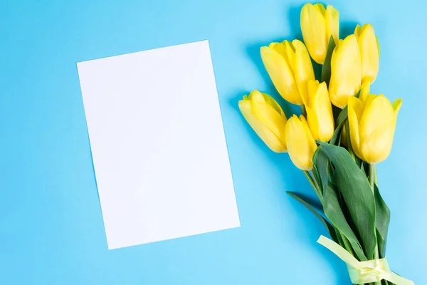 Bouquet de belles tulipes jaunes fraîches sur fond bleu et carte blanche pour le texte — Photo