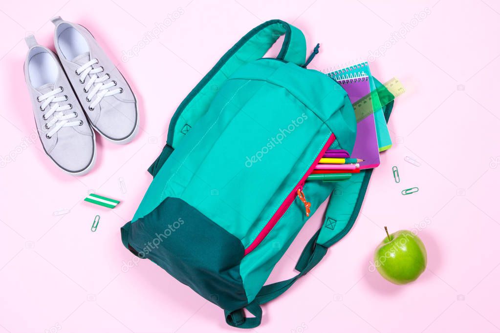 Backpack with school stationery on pink background
