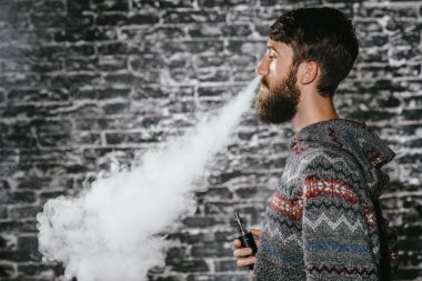 Elektronik sigara içen sakallı genç adam. Vaper hipster duman buharlaştırıcı..