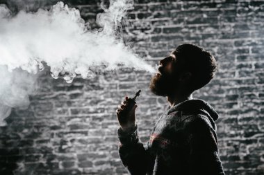 Elektronik sigara içen sakallı genç adam. Vaper hipster duman buharlaştırıcı..