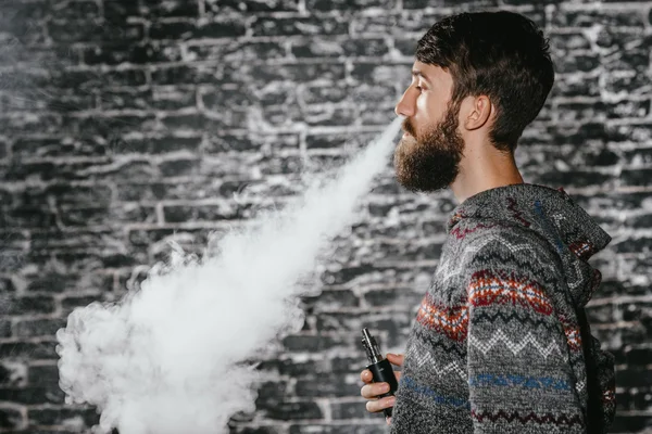 Elektronik sigara içen sakallı genç adam. Vaper hipster duman buharlaştırıcı..