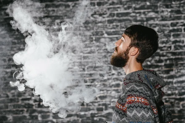 Młody człowiek z brodą wymiotujący elektronicznym papierosem. Vaper hipster dymu parownik. — Zdjęcie stockowe