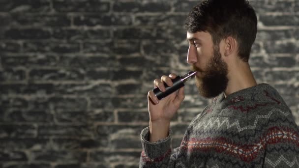 Молодой человек с бородой выкуривает электронную сигарету. Парящий испаритель хипстерского дыма в замедленной съемке — стоковое видео