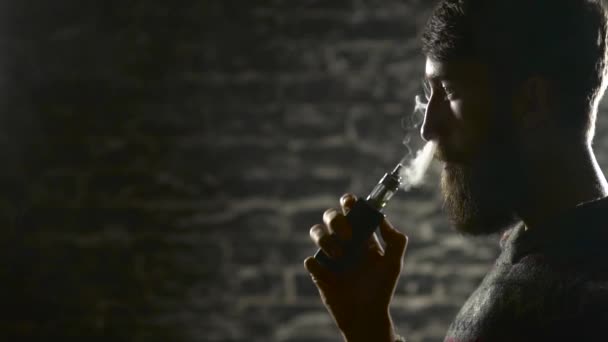 Молодой человек с бородой выкуривает электронную сигарету. Парящий испаритель хипстерского дыма в замедленной съемке — стоковое видео