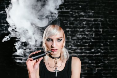 Seksi goth kız koyu arka plan üzerinde elektronik sigara içiyor. Model vaper vaping bir Buharlaştırıcı stüdyo.
