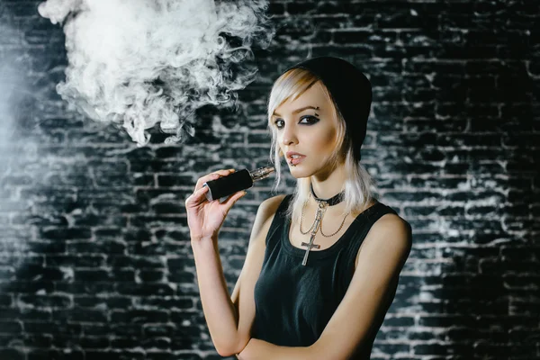 Sexy chica gótica fuma cigarrillo electrónico sobre fondo oscuro. El modelo vaper vapeando un vaporizador en el estudio . — Foto de Stock