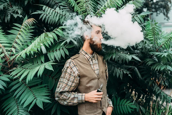 Jovem com barba vaporizando um cigarro eletrônico ao ar livre. vaporizador de fumo hipster . — Fotografia de Stock