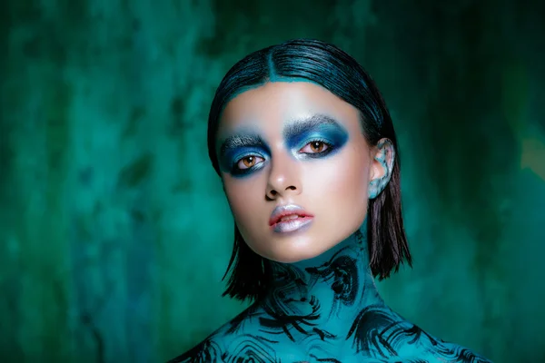 Make-up Art v jasných barvách. Krásná brunetka v krátké vlasy pózuje v ateliéru na tyrkysové pozadí. Zářivou pokožku — Stock fotografie