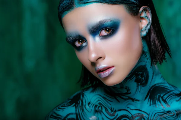 Make-up Art v jasných barvách. Krásná brunetka v krátké vlasy pózuje v ateliéru na tyrkysové pozadí. Zářivou pokožku — Stock fotografie