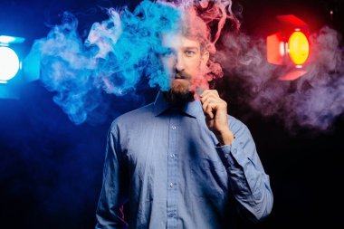 Young guy with a beard vaping and releases a cloud of vapor. hipster vaper smoke vaporizer. clipart