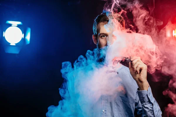 Un joven con barba vapeando y libera una nube de vapor. vaporizador de humo hipster vaper . — Foto de Stock