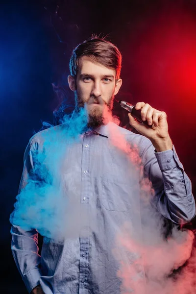 Un joven con barba vapeando y libera una nube de vapor. vaporizador de humo hipster vaper . — Foto de Stock