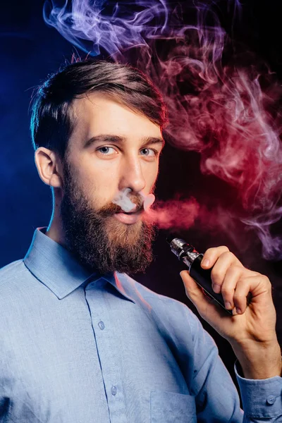 Un joven con barba vapeando y libera una nube de vapor. vaporizador de humo hipster vaper . — Foto de Stock