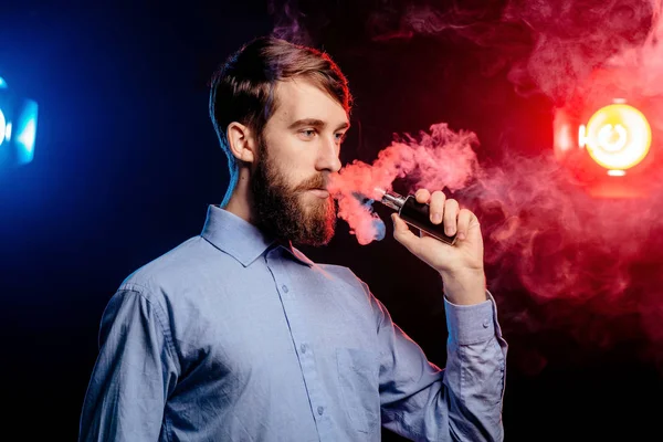 Un joven con barba vapeando y libera una nube de vapor. vaporizador de humo hipster vaper . — Foto de Stock