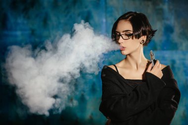 Bir kızla gözlük vaping ve Buhar bulutu serbest bırakır. Turkuaz bir arka plan üzerinde siyah vaper duman Buharlaştırıcı model