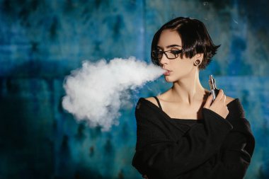 Bir kızla gözlük vaping ve Buhar bulutu serbest bırakır. Turkuaz bir arka plan üzerinde siyah vaper duman Buharlaştırıcı model