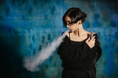 Bir kızla gözlük vaping ve Buhar bulutu serbest bırakır. Turkuaz bir arka plan üzerinde siyah vaper duman Buharlaştırıcı model