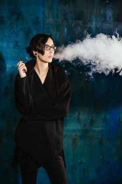 Bir kızla gözlük vaping ve Buhar bulutu serbest bırakır. Turkuaz bir arka plan üzerinde siyah vaper duman Buharlaştırıcı model