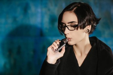 Bir kızla gözlük vaping ve Buhar bulutu serbest bırakır. Turkuaz bir arka plan üzerinde siyah vaper duman Buharlaştırıcı model