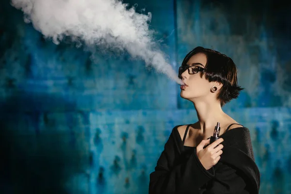Dziewczyna z vaping okulary i wypuszcza chmurę pary wodnej. Model w internetowych czarny dym odparowalnik na turkus tło — Zdjęcie stockowe