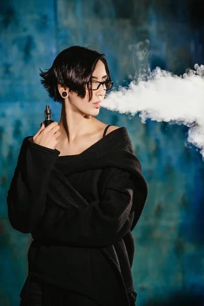 Dziewczyna z vaping okulary i wypuszcza chmurę pary wodnej. Model w internetowych czarny dym odparowalnik na turkus tło — Zdjęcie stockowe