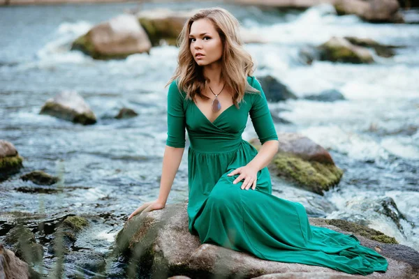 Красивая девушка позирует на камнях у воды. Модель в зеленом платье в природе . — стоковое фото