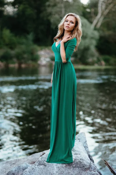 Beautiful girl posing on rocks near the water. Model in a green dress in nature. — Stock Photo, Image