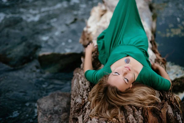 Belle fille posant sur des rochers près de l'eau. Modèle dans une robe verte dans la nature . — Photo