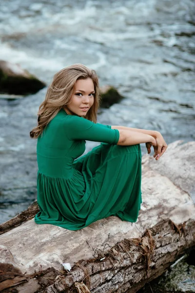 Piękna dziewczyna pozuje na skały w pobliżu wody. Model w zieloną sukienkę w przyrodzie. — Zdjęcie stockowe