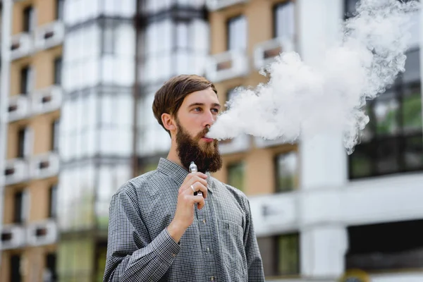 Men model with beard vaping an electronic cigarette. Vaping outdoors. Safe smoking. Young hipster vaper.