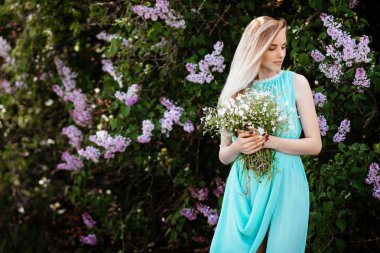 Kır çiçekleri açık havada A model turkuaz elbise Lila bush çerçevede bir buket ile sarışın kız.