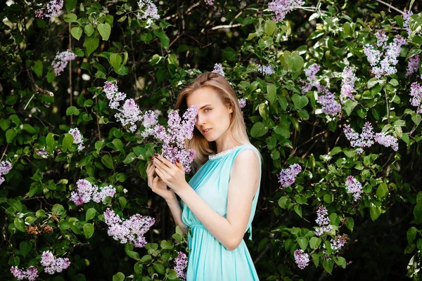 Blondynka z bukiet kwiaty dzikiego plenerze modelu w turkusową sukienkę na tle krzak bzu. — Zdjęcie stockowe