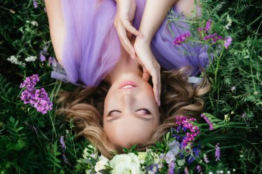 Güzel kız manken çim yalan portresi. Mor çiçekli bir çelenk içinde gelin. Yukarıdan görüntülemek.